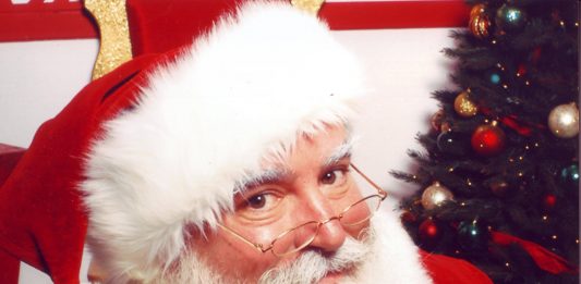 hombre vestido de papa noel sentado al lado de un arbol de navidad