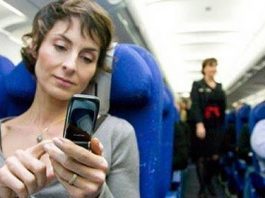 mujer con el pelo corto en el asiento azul de un avion usando el movil