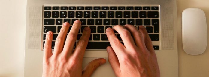 manos sobre teclado de un ordenador portatil en una mesa blanca de una oficina tecleando
