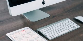 apple mac y una tablet en pantalla un calendario sobre una mesa de madera de una oficina