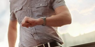 hombre con camisa beige en un puente de madera mirando su reloj de pulsera