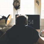 hombre con camiseta en un estudio sentado de espaldas frente al ordenador trabajando