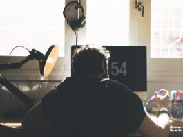 hombre con camiseta en un estudio sentado de espaldas frente al ordenador trabajando