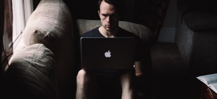 hombre serio en una casa sentado en el sofa mirando el ordenador portatil