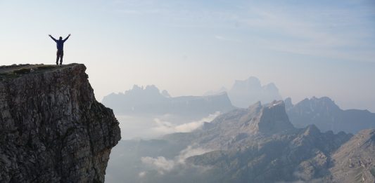 persona con una mochila en la cima de una montaña levantando los brazos mirando las montañas
