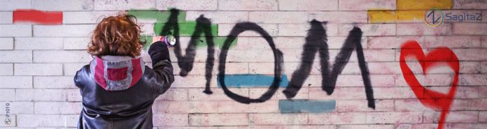 chico joven con chaqueta de cuero en la calle de espaldas grafiteando en una pared la palabra mom