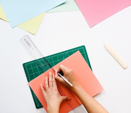 Manos en una mesa de una oficina con una cartulina regla y lapiz dibujando