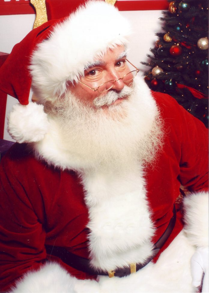 hombre vestido de papa noel sentado al lado de un arbol de navidad