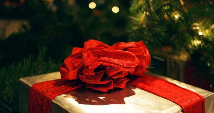 regalo dorado con lazo rojo en el salon de una casa con el arbol de navidad al fondo