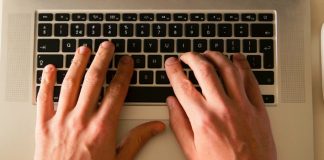 manos sobre teclado de un ordenador portatil en una mesa blanca de una oficina tecleando