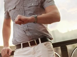 hombre con camisa beige en un puente de madera mirando su reloj de pulsera