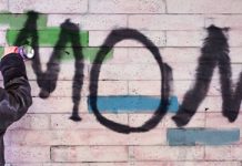 chico joven con chaqueta de cuero en la calle de espaldas grafiteando en una pared la palabra mom